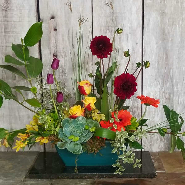 Mixed floral arrangement with red, orange, yellow, and purple blooms in a teal container