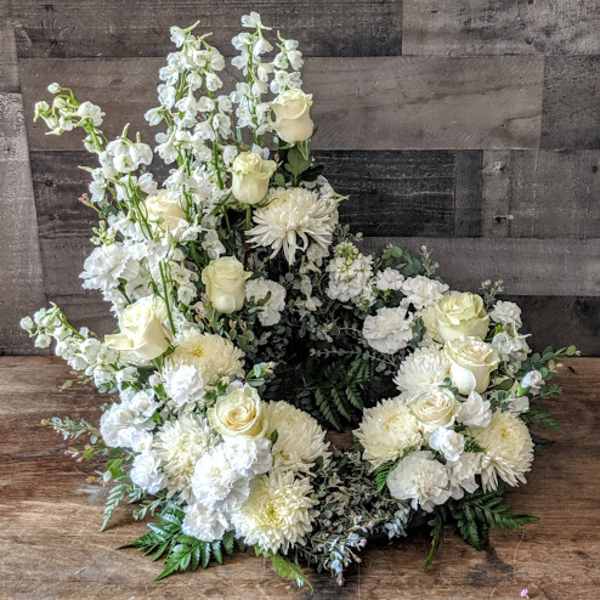 Open wreath of white and cream roses, mums, carnations, and tall white blooms arranged asymmetrically