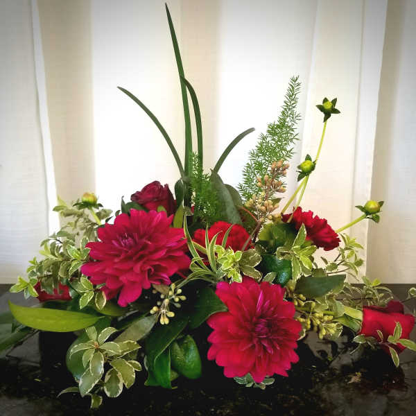 Low floral arrangement with magenta blooms and red roses in a dark container