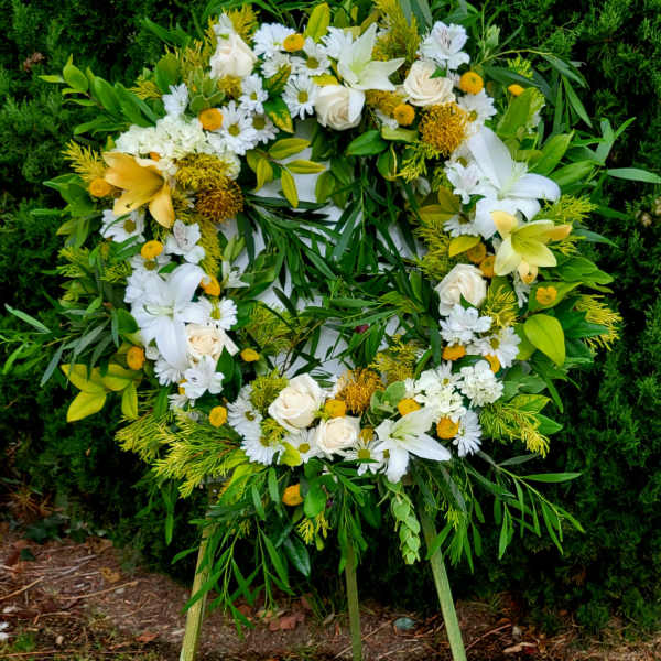 Circular standing wreath of white and yellow flowers on an easel