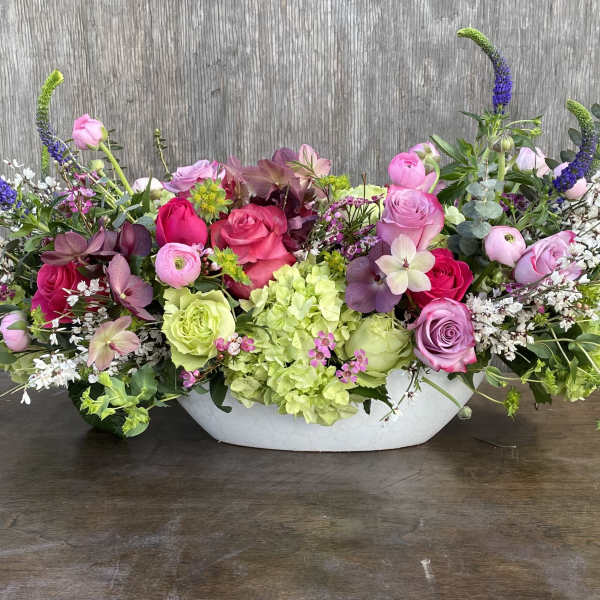 Low floral centerpiece with pink and purple roses in a white bowl vase