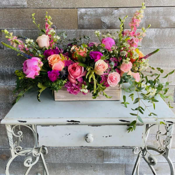 Long floral arrangement with pink and peach roses in a wooden box