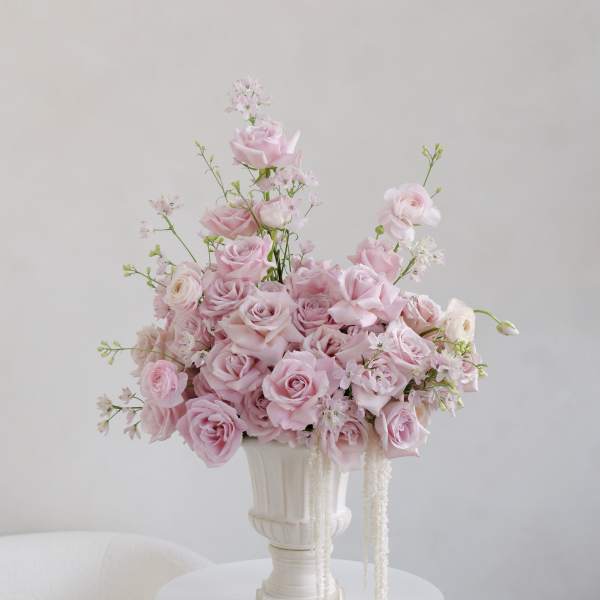 Pink rose arrangement in a white pedestal vase