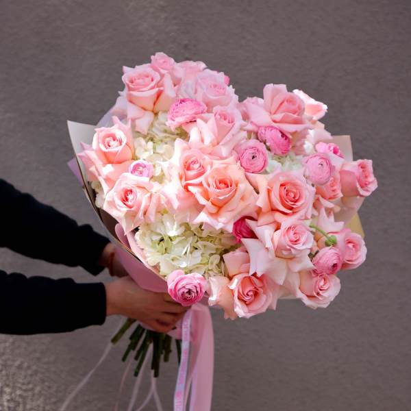 Handheld bouquet of pink roses and pale flowers wrapped with pink ribbon