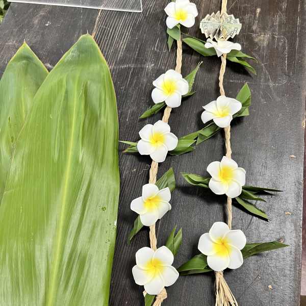 Two floral garlands with white plumeria flowers and green leaves on a dark surface