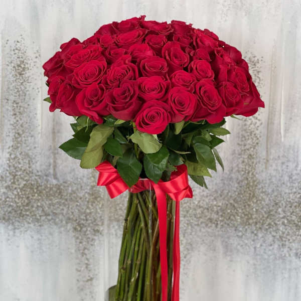 Tall bouquet of red roses in a glass vase with a red ribbon