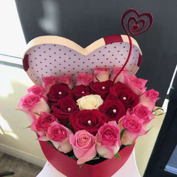 Heart-shaped box of pink and red roses with a decorative heart topper