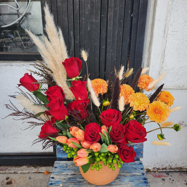 Red roses and orange flowers in a peach vase with dried grasses