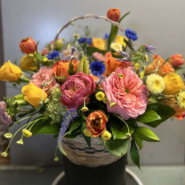 Basket arrangement of pink and yellow flowers with blue accents