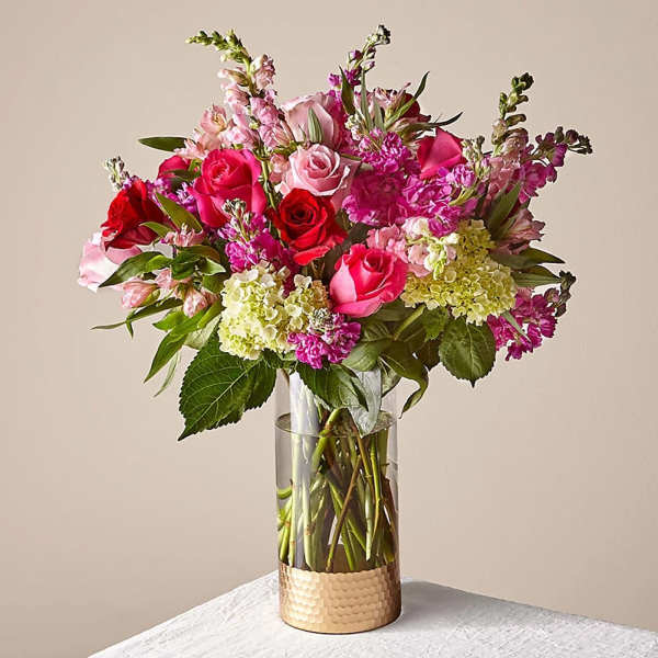 Pink and red roses with mixed blooms in a clear glass vase