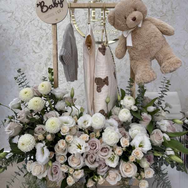 Baby shower floral display with a teddy bear and hanging baby clothes