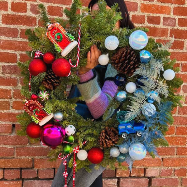 Person holding a decorated Christmas wreath with ornaments and pinecones