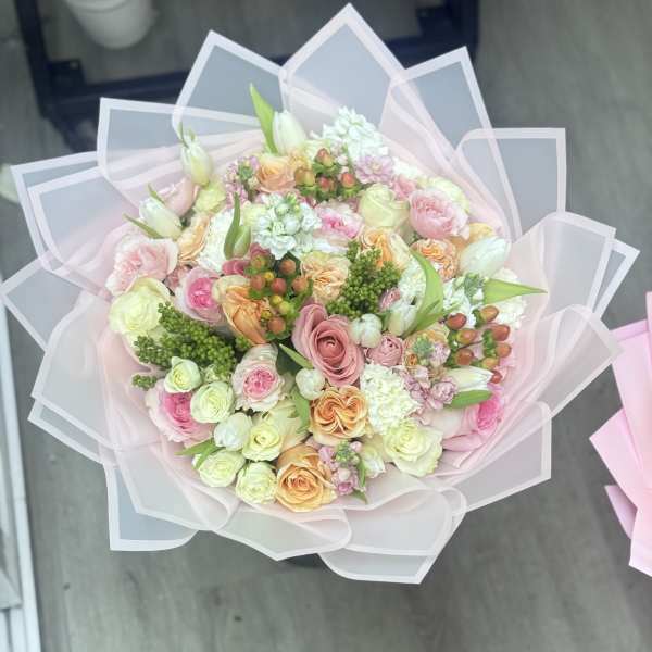 Pastel bouquet of roses and mixed blooms wrapped in translucent pink paper