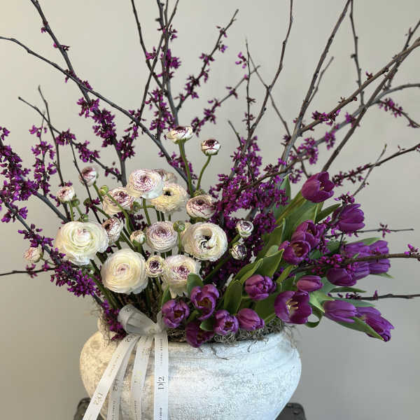 Purple tulips and white ranunculus in a textured vase with branches