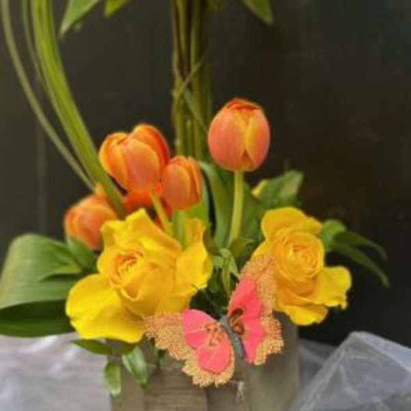 Yellow and orange floral arrangement in a square container with butterfly accents