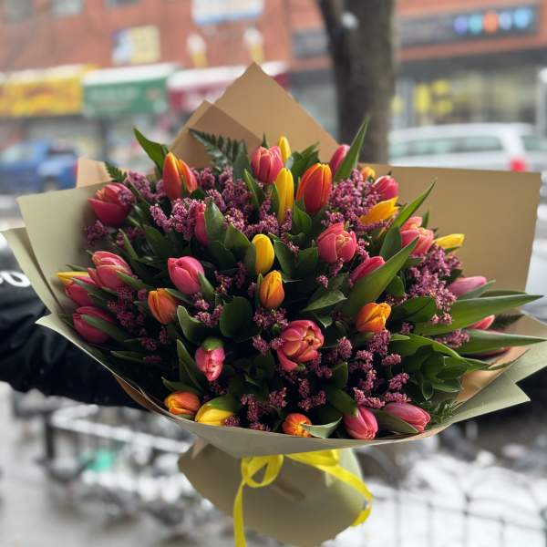 Bouquet of pink and yellow tulips wrapped in paper with a yellow ribbon