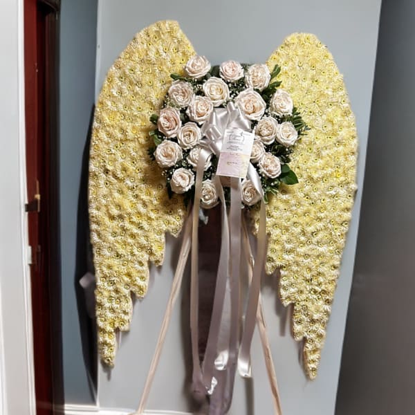 Standing floral tribute with pale roses and yellow flower wings on an easel