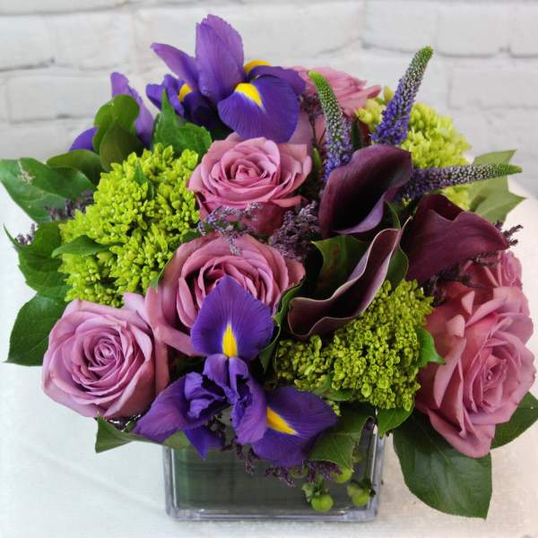 Bouquet of pink roses, purple irises, and green blooms in a glass vase