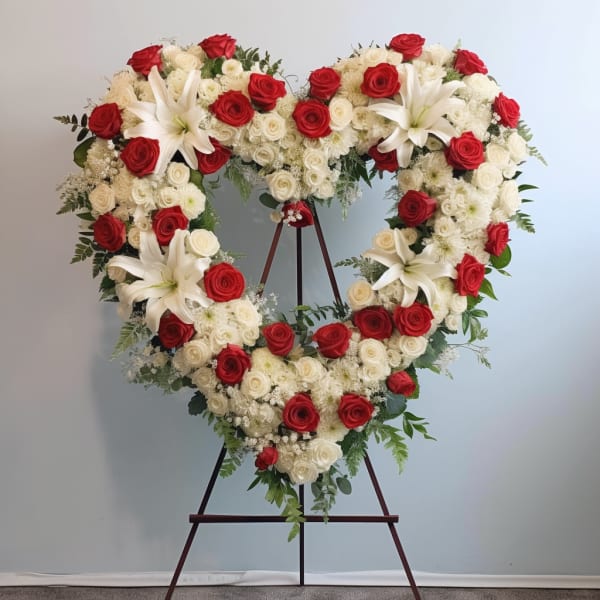 Heart-shaped floral wreath of red and white roses with white lilies on an easel