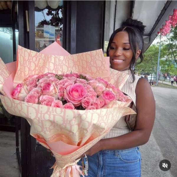 Woman holding a large bouquet of pink roses wrapped in patterned paper