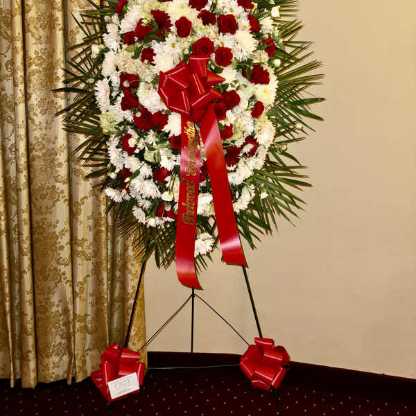 Standing floral wreath of red and white flowers with a red ribbon