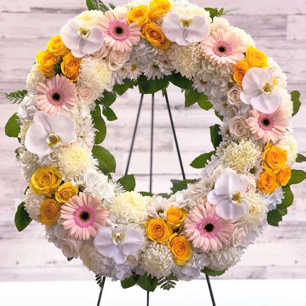Circular floral wreath with white, pink, and yellow blooms on a stand
