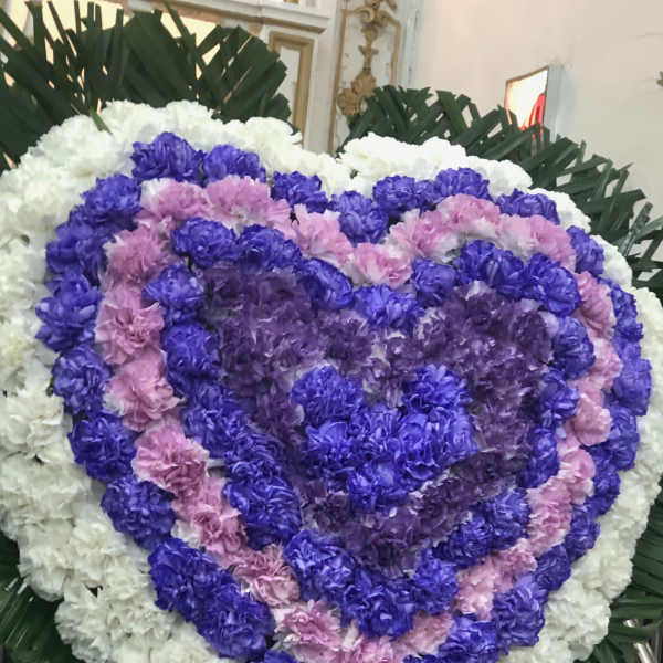 Heart-shaped floral wreath in white, purple, and pink flowers with a purple ribbon