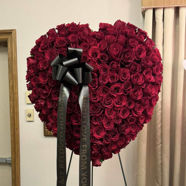 Heart-shaped arrangement of red roses with a black ribbon bow