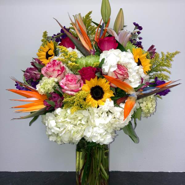 Colorful mixed bouquet in a clear glass vase with sunflowers, roses, lilies, and hydrangeas