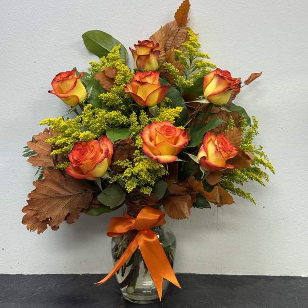 Orange and yellow roses in a glass vase with an orange ribbon