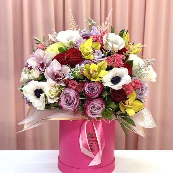 Mixed bouquet of roses, orchids, and anemones in a pink hat box