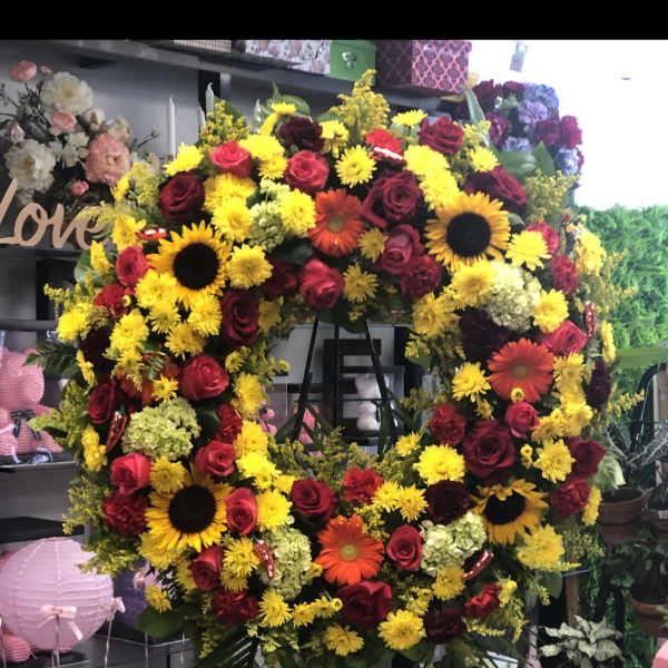 Large floral wreath with red roses, yellow blooms, and sunflowers on a stand