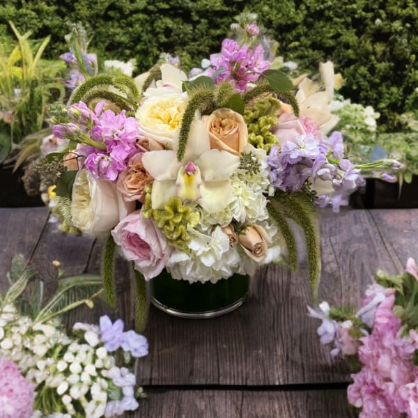 Mixed pastel bouquet in a dark green vase with roses and orchids