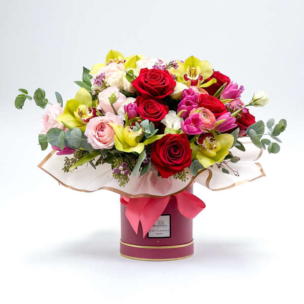 Bouquet of red roses, pink blooms, and yellow orchids in a round box