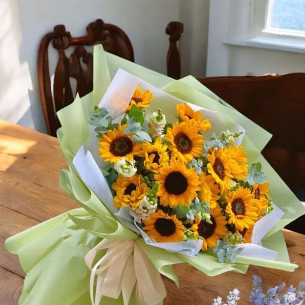 Bouquet of sunflowers wrapped in pale green paper with a cream ribbon