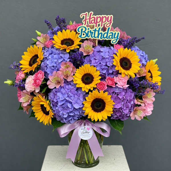 Colorful birthday bouquet with sunflowers, hydrangeas, and pink flowers in a glass vase