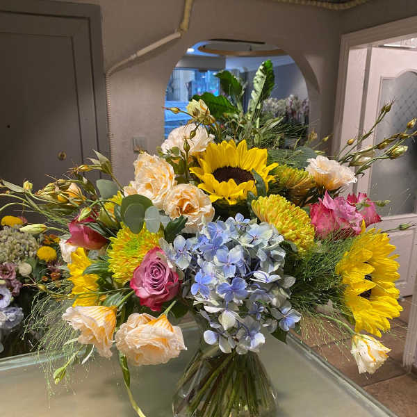 Mixed bouquet with sunflowers, roses, hydrangea, and carnations in a glass vase