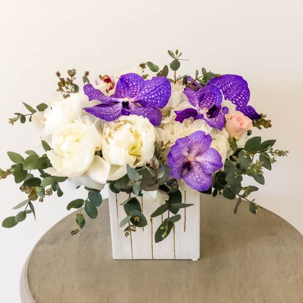 White and purple floral arrangement in a white wooden box