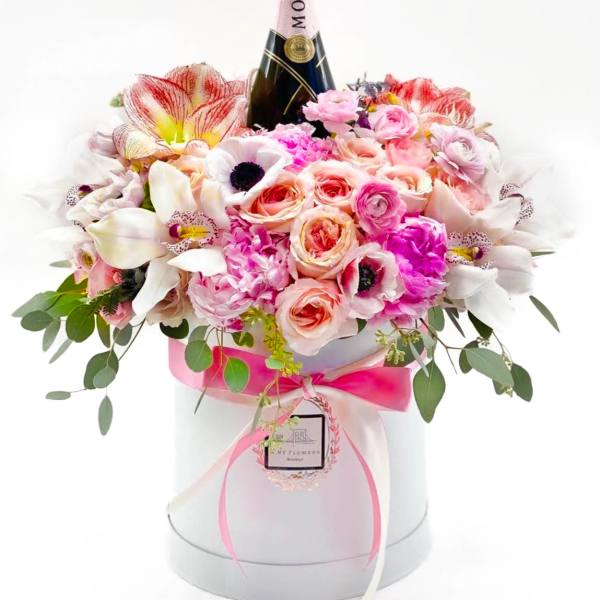 Pink and white flower arrangement in a round box with a Moët bottle