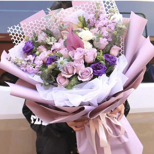 Large bouquet of pink and purple flowers wrapped in pastel paper