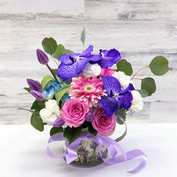 Pink and purple mixed bouquet in a decorative tin container with ribbon