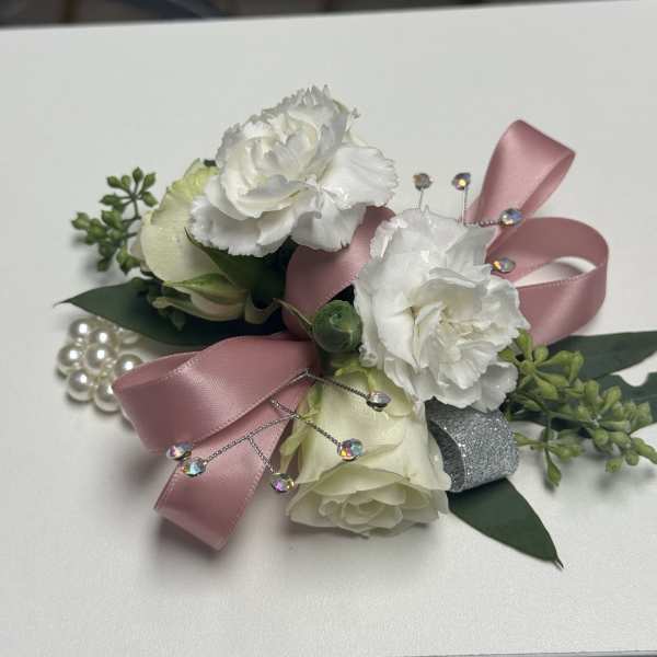 White carnation and rose wrist corsage with pink ribbon, pearls, and crystal accents on a white surface