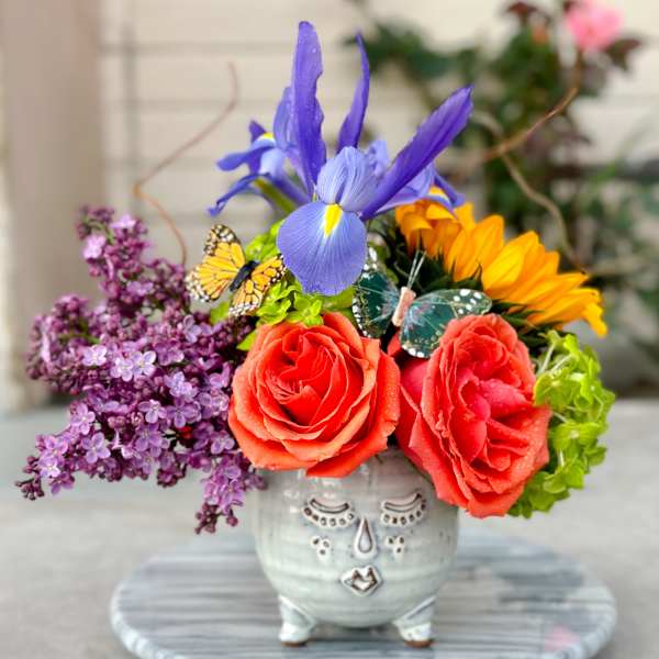 Colorful bouquet in a decorative ceramic face vase with roses and iris