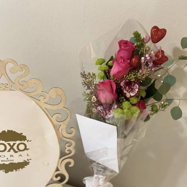 Bouquet of pink roses and green button mums with heart picks in a clear vase