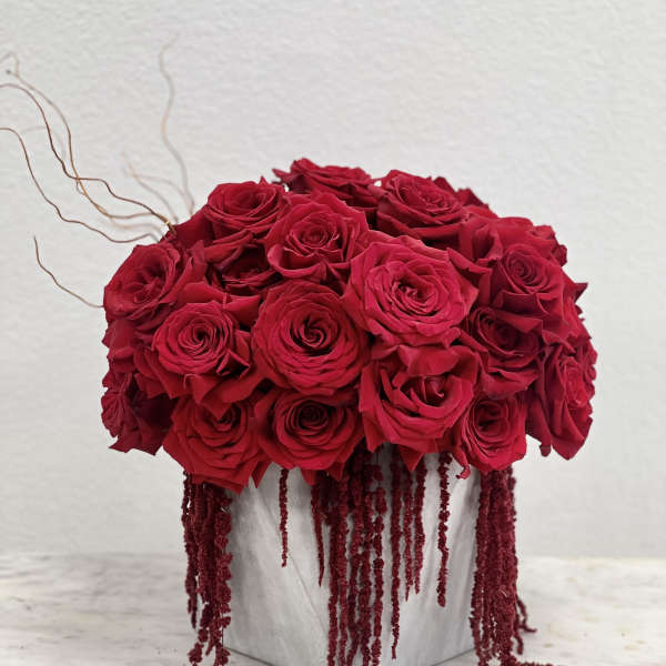 Compact arrangement of red roses with trailing red accents in a gray cube vase on a small table