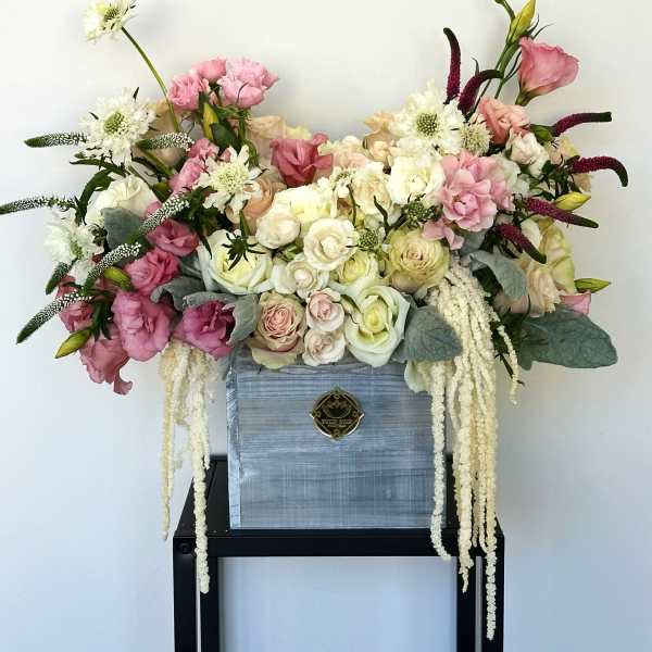 Large pastel floral arrangement in a blue box with trailing white blooms