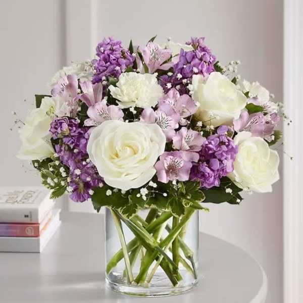 White roses and purple flowers arranged in a clear glass vase