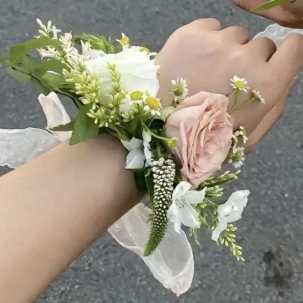 Two wrists wearing small floral corsages with pink and white flowers