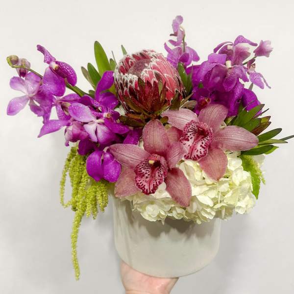 Purple orchids and pink protea in a white vase