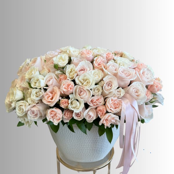 Large bouquet of pale pink and white roses in a white vase with a pink ribbon